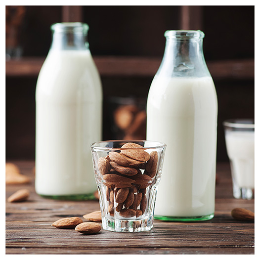 Bottiglie e bicchieri di latte fresco con mandorle sul tavolo in legno.